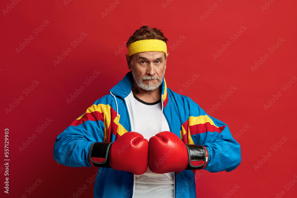 Strong Man Boxing In Gloves. Portrait of Senior Man Training And Demonstrating Power in His Hands, Feeling Energy In His Age. Indoor Studio Shot Isolated on Red Background Strong Man Boxing In Gloves. Portrait of Senior Man Training And Demonstrating Power in His Hands, Feeling Energy In His Age. Indoor Studio Shot Isolated on Red Background
