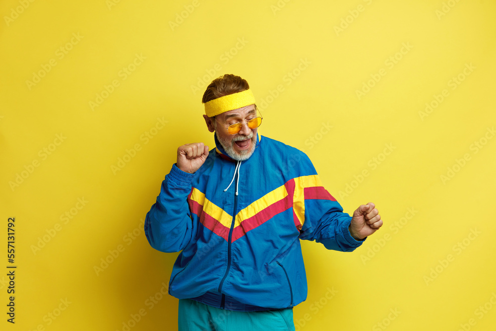 Senior Man Dancing Isolated. Portrait of Ecstatic Overjoyed Grandfather Dancing with Raised Arms, Smiling Excitedly, Celebrating Victory, Success. Indoor Studio Shot Isolated on Yellow Background 