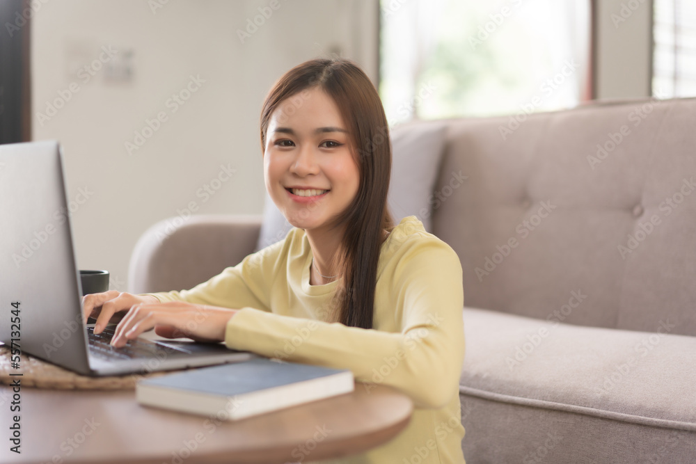 Concept of activity in home, Young woman is typing on laptop and smiling while sitting on the floor Concept of activity in home, Young woman is typing on laptop and smiling while sitting on the floor