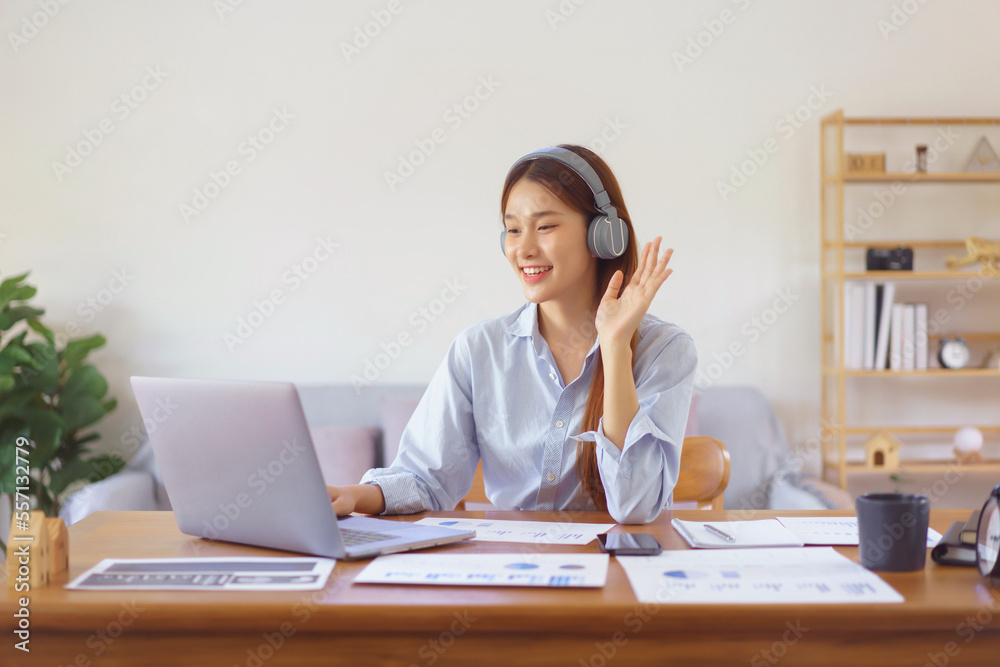 Home office concept, Businesswoman wears headphone to meeting and greeting colleague in video call Home office concept, Businesswoman wears headphone to meeting and greeting colleague in video call