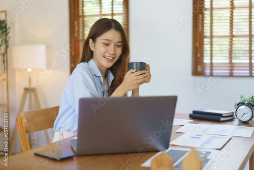 Business at home concept, Businesswoman reading marketing plan data on laptop and drinking coffee