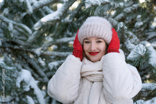 Girl is enjoying frosty winter day in the park. Portrait of young woman on snowy pine trees background.