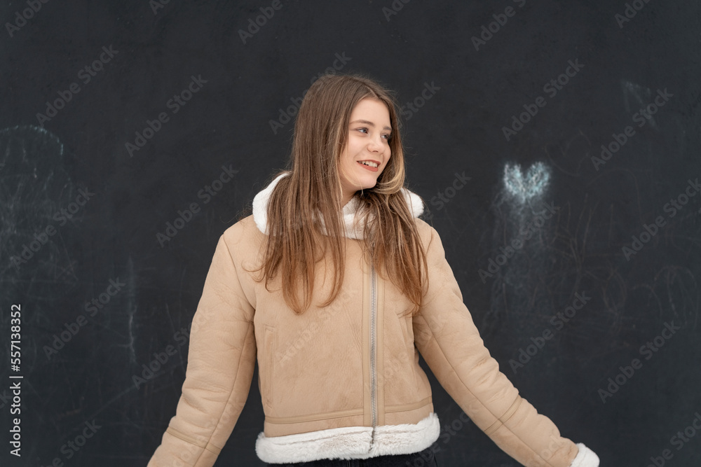 Portrait of young woman on black background in beige sheepskin coat posing in studio. Girl in warm outerwear