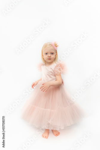 Little barefoot girl wears pink dress with satin skirt. Happy princess in festive outfit on white background. Vertical frame