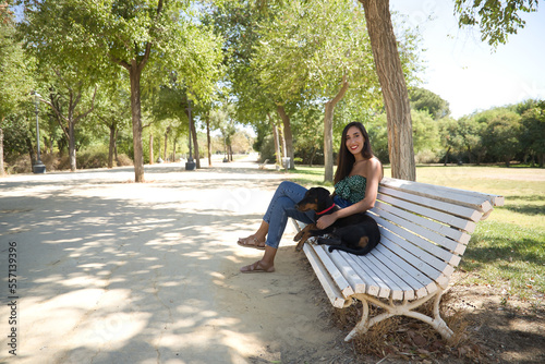 Young woman, brunette, slender, dressed in green t-shirt and jeans, sitting on a bench next to her dog, happy and in a loving attitude. Concept animals, pets, friends, love, dogs, breed.