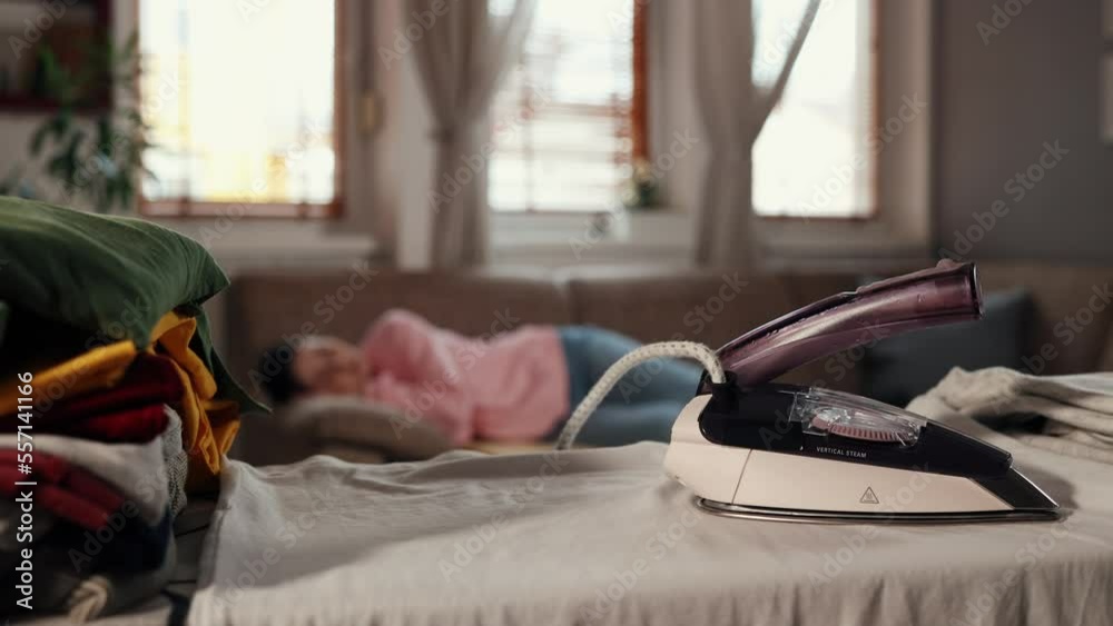 Housewife sleeps on sofa, forgetting about hot iron left ironing board. Iron close-up. Home interior. Housewife sleeps on sofa, forgetting about hot iron left ironing board. Iron close-up. Home interior.