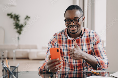 African american man shows thumb up hand gesture, holding phone smiling. Positive feedback gesture