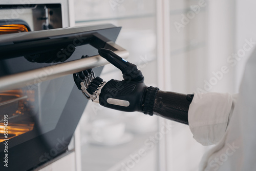 Robotic cyber hand of disabled person is opening oven at kitchen. Amputee is cooking.