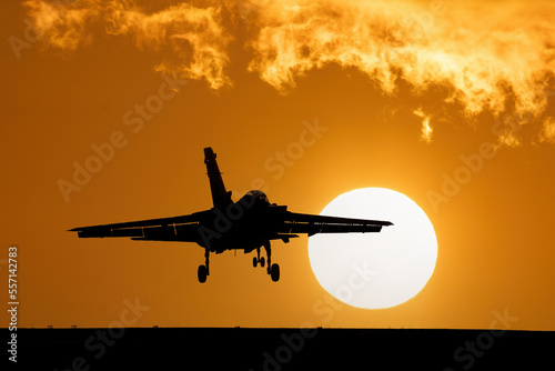 Fighter jet at sunset with orange sky and large setting sun after a combat mission. Flying over dramatic silhouette of fighter bomber jet aircraft