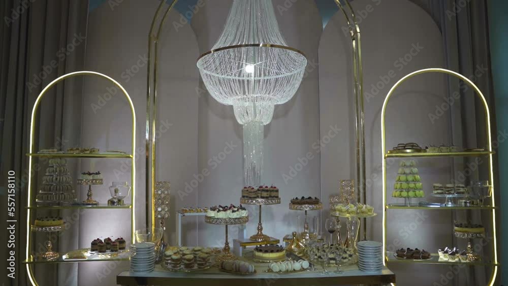 Stylish candy bar in gold colours. Sweet cakes and candies with muffins. People have fun and rest on the event. Beautiful festive decoration. Decor on the evening party. Stylish candy bar in gold colours. Sweet cakes and candies with muffins. People have fun and rest on the event. Beautiful festive decoration. Decor on the evening party.