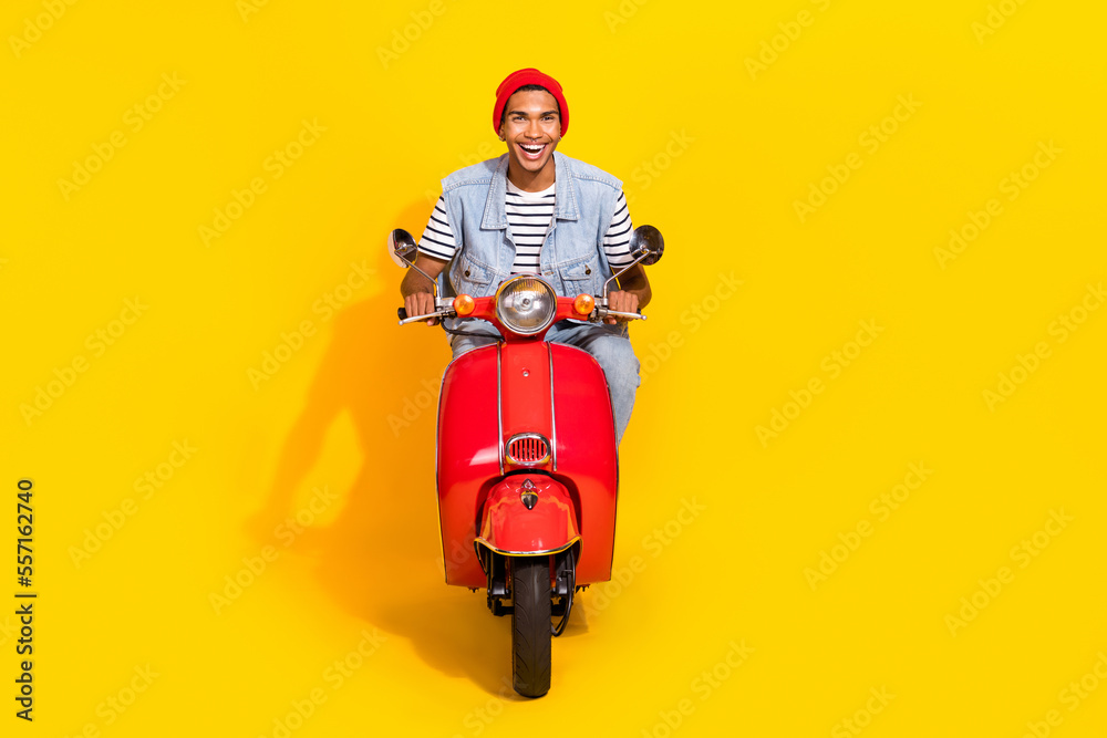 Full length photo of cheerful positive man wear jeans outfit riding moped smiling isolated yellow color background Full length photo of cheerful positive man wear jeans outfit riding moped smiling isolated yellow color background