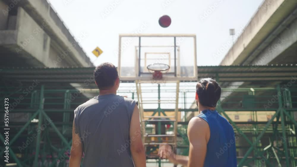 Two man athlete playing streetball match shooting and defense basketball on outdoors court together in sunny day. Sportsman do sport training basketball at street court under highway in the city. Two man athlete playing streetball match shooting and defense basketball on outdoors court together in sunny day. Sportsman do sport training basketball at street court under highway in the city.