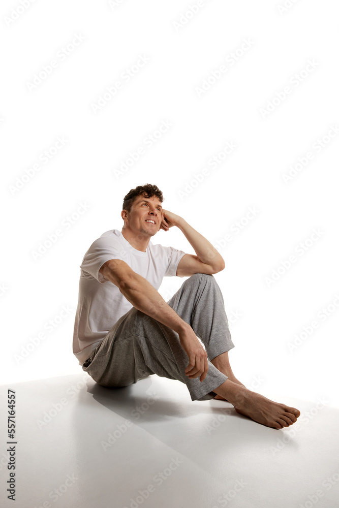 Relaxed look. Mature smiling man sitting on floor in T-shirt and pants over white studio background. Homewear. Comfort. Men's health and beauty Relaxed look. Mature smiling man sitting on floor in T-shirt and pants over white studio background. Homewear. Comfort. Men's health and beauty
