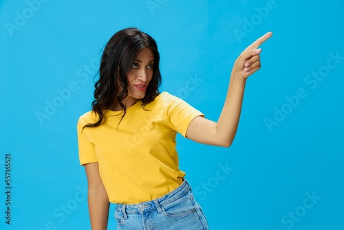 Woman in yellow t-shirt on blue background posing gestures emotions and signals with smile, hands up happiness copy space