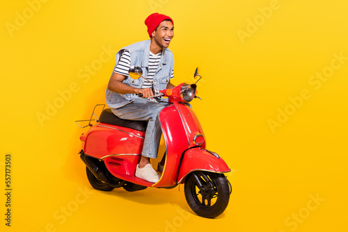 Full length photo of cute excited man wear jeans outfit riding moped looking empty space isolated yellow color background © deagreez