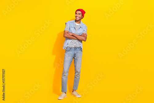 Full length photo of cheerful dreamy man wear jeans outfit looking empty space arms crossed isolated yellow color background