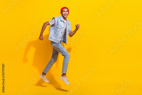 Full length photo of funky excited man wear jeans outfit jumping high running empty space isolated yellow color background