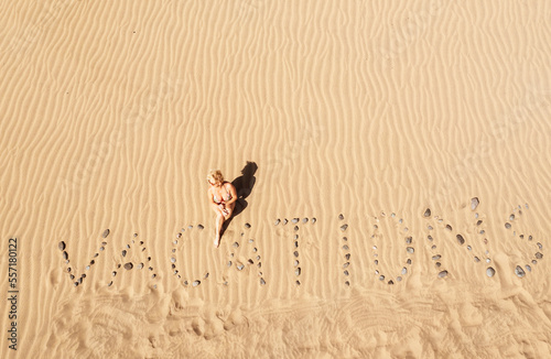 View from above to the dunes with word "vacations". Summer holidays background. Woman posing near text"VACATIONS" in a sandy beach. VACATIONS concept 