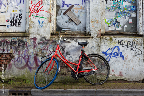 Red bicycle with blue tyre parked in an alley with graffiti