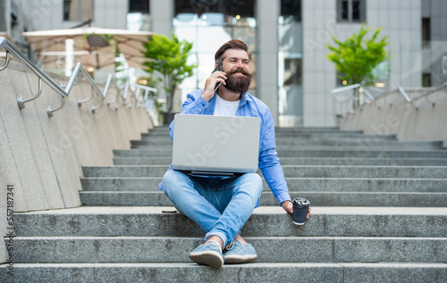 Happy man talking on mobile phone drinking coffee relaxing on stairs. Smiling man making mobile call