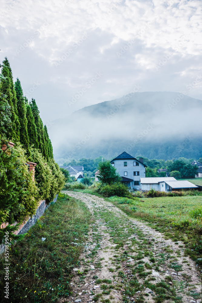 Mountain from view with small village and flow fog. Foggy summer morning in the mountains and a small village. Country road in the mountains. Carpathians. Polyana. Ukraine