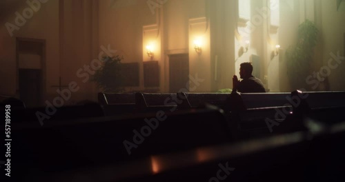 Wide Shot of Devout Christian Man Sits Piously In a Church, Folding Hands For Praying, Seeks Guidance From His Religious Faith and Spirituality. Spirit of Christianity and Hope for Repentance