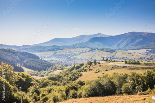 View from a mountain to a valley between mountains with a river and a village on a summer day. View over the hills, mountains, valley, river and village. Carpathians. Ukraine