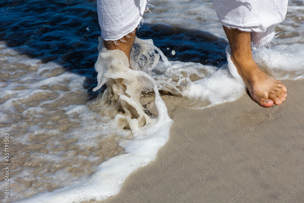 Man in white Jesus-type robe showing legs in sea