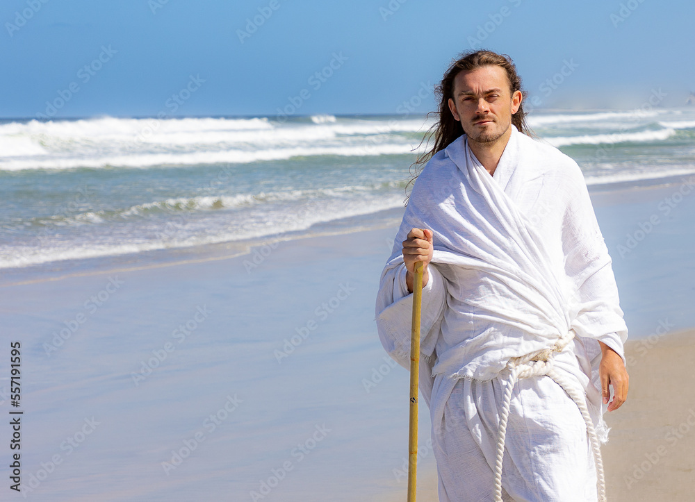 Man in white robe walks near sea with a staff