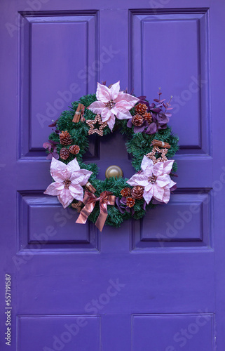 Christmas wreath with bright flowers on door of purple color