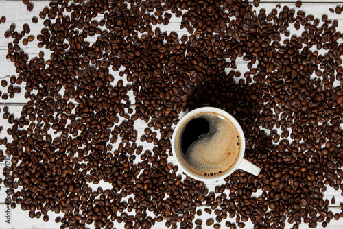 Ziarna kawy rozsypane na stole.  Filiżanka gorącej czarne kawy z pianką. Tło z ziaren kawy. © art08
