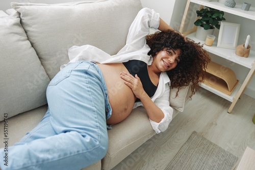 Pregnant woman smile and happiness lies on the couch freedom and strokes her belly feels kicks with the baby in the last month of pregnancy, mother's day lifestyle