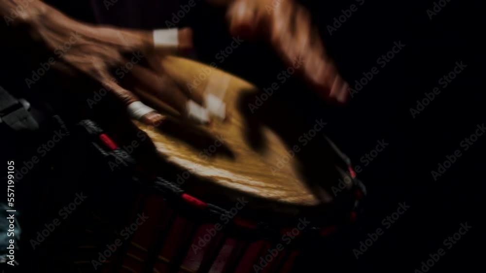 Close up of African man hands drumming on bongo in slow motion. Authentic traditional musical instrument. Musical performance in black studio
