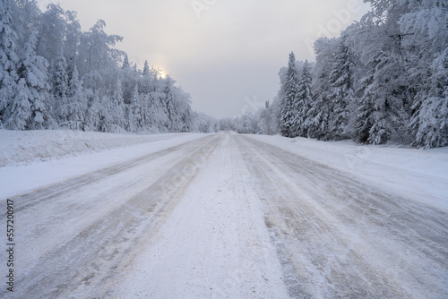 Snow and ice covered road that disappears into the distance and is surrounded by a snowy forest. 