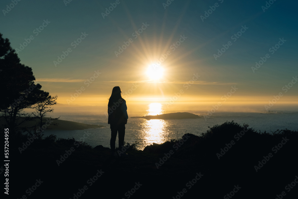 Silhouette of a young woman on a cliff in Monteferro at sunset. Nigran - Spain