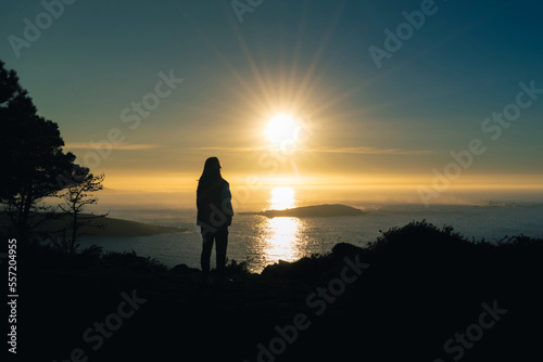 Silhouette of a young woman on a cliff in Monteferro at sunset. Nigran - Spain
