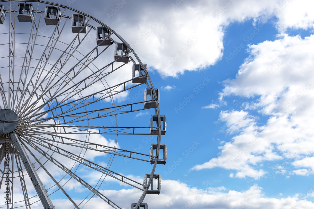 Round Ferris wheel and light blue sky with white clouds
