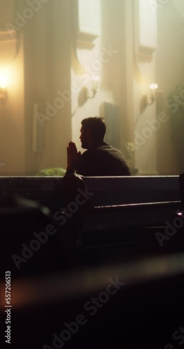 Young Christian Man Sits Piously in Majestic Church, with Folded Hands He Seeks Guidance From Faith and Spirituality while Praying. Religious Believer in the Great Power and Love of God. Slow Motion  photo