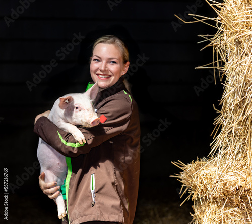 Junge Frau mit schwerem Ferkel im Arm vor einem schwarzen Hintergrund, an der Seite sind Strohbunde zu erkennen. photo