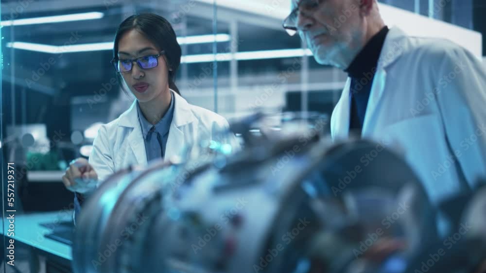 Diverse Multiethnic Team of Industrial Engineers Gathered Around a Table With a Prototype Turbofan Engine. Scientists Discuss the Futuristic Motor, Use Equipment and Tablet Computer for Research. Diverse Multiethnic Team of Industrial Engineers Gathered Around a Table With a Prototype Turbofan Engine. Scientists Discuss the Futuristic Motor, Use Equipment and Tablet Computer for Research.