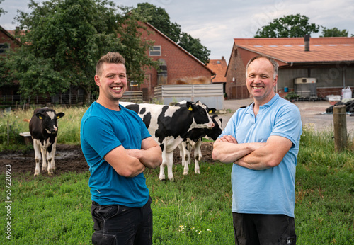 Landwirt mit seinem Sohn auf einer Wiese, im Hintergrund Rinder und ein Hof. photo