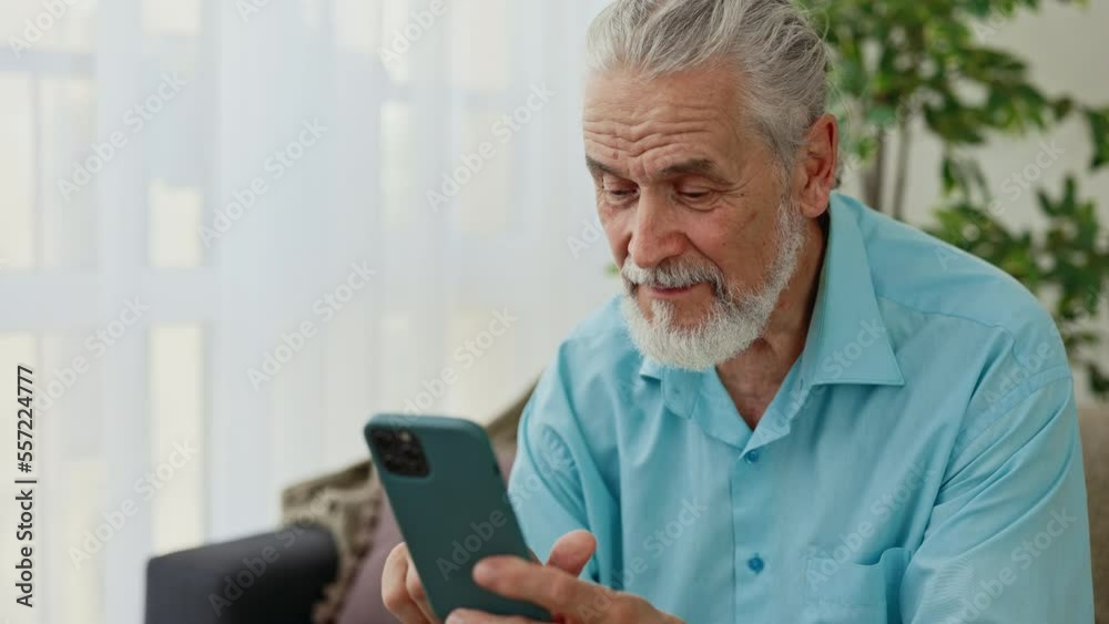 Close view of the happy mature caucasian man sitting on the sofa and using smartphone. Senior male pensioner is chatting on the social media. Technology and communication concept Close view of the happy mature caucasian man sitting on the sofa and using smartphone. Senior male pensioner is chatting on the social media. Technology and communication concept