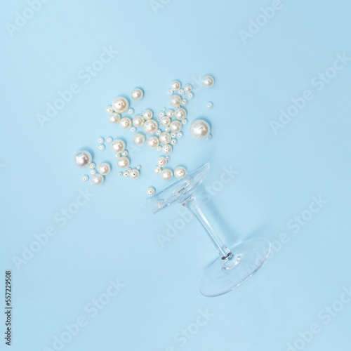 Broken cocktail glass and shinny pearl beads, creative aesthetic champagne concept against pastel blue background. Minimal celebration idea. 
