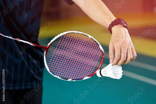 Badminton player holds racket and white cream shuttlecock in front of the net before serving it to another side of the court. © Sophon_Nawit