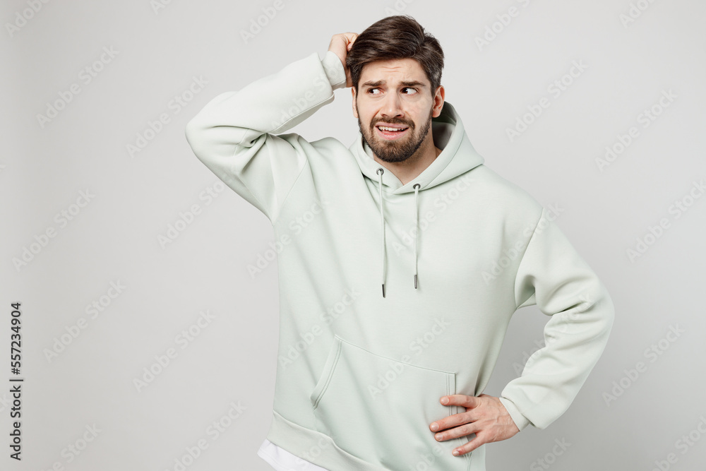 Young confused mistaken sad puzzled unshaven caucasian man wearing mint hoody look aside on workspace area mock up isolated on plain solid white background studio portrait. People lifestyle concept Young confused mistaken sad puzzled unshaven caucasian man wearing mint hoody look aside on workspace area mock up isolated on plain solid white background studio portrait. People lifestyle concept