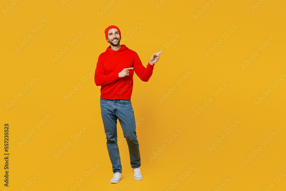 Fototapeta premium Full body fun young man wear red hoody hat point index finger aside indicate on workspace area copy space mock up isolated on plain yellow color background studio portrait. People lifestyle concept.