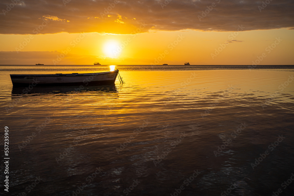 Baie-du-Tombeau Mauritius Sunset over the bay with single fishing boat sloop in foreground and horizon showing large scale fishing boards silhouetted in the background