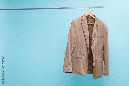 Brown jacket hanging on a hanger over blue background with copy space.
