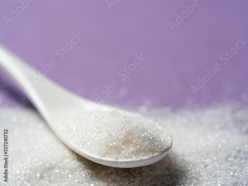 Sugar in white spoon on violet, copy space
