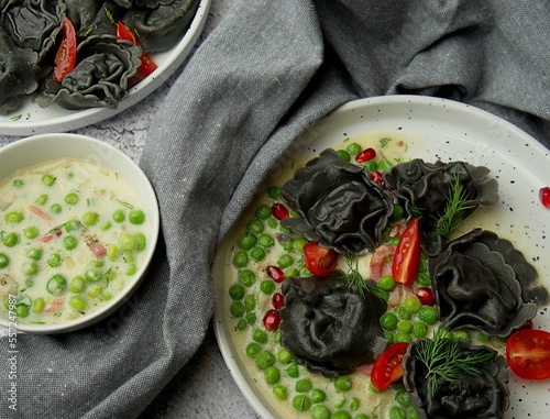 Czarne ravioli z zielonym groszkiem boczkiem i pomidorkami photo